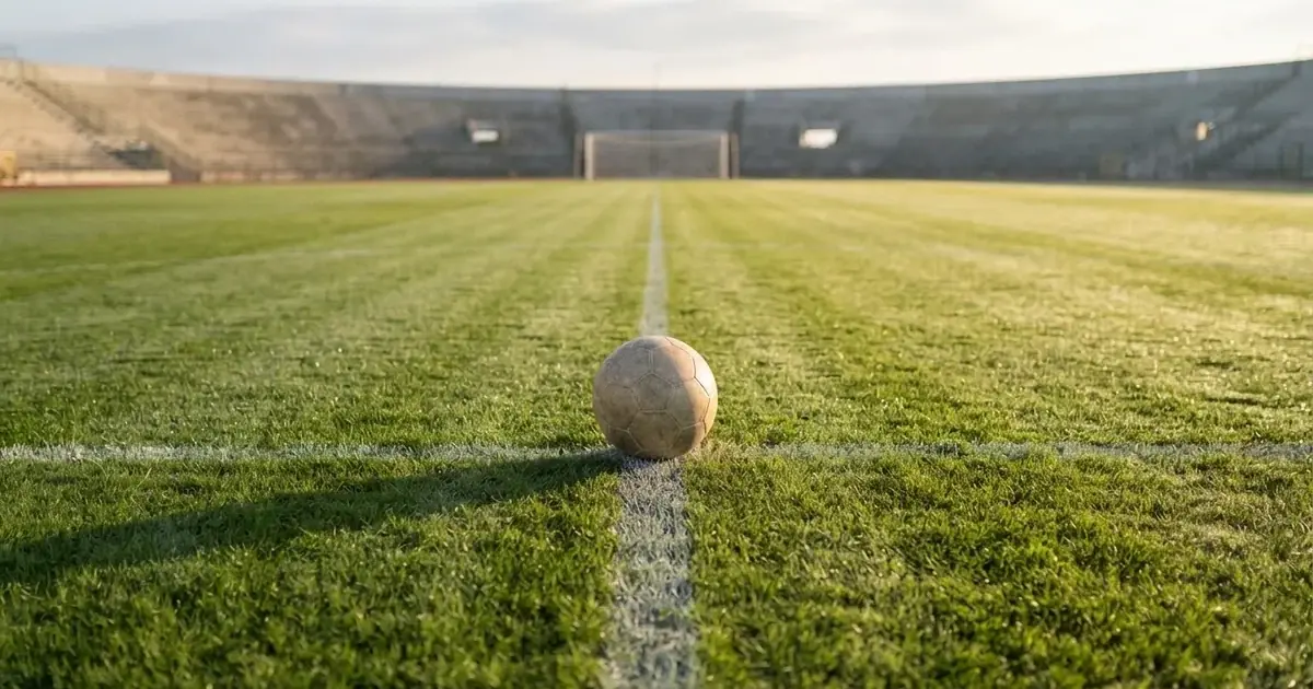 Een voetbal op de middenstip van een grasveld in het ochtendlicht