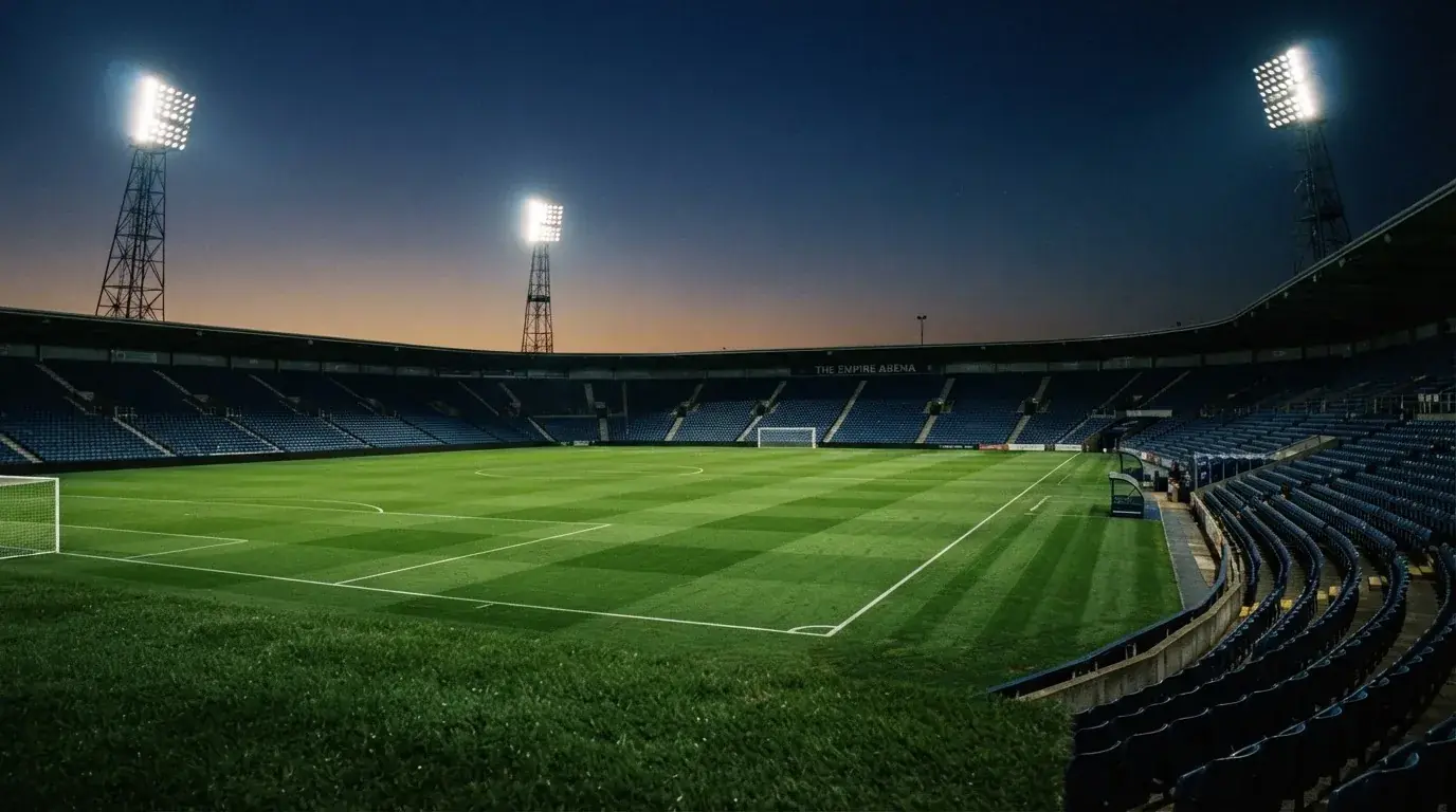Een leeg voetbalstadion met lichtmasten bij schemering