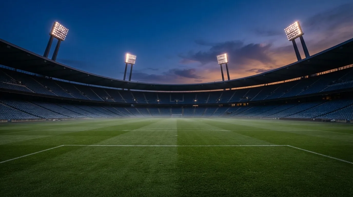 Een leeg voetbalstadion met lichtmasten bij schemering